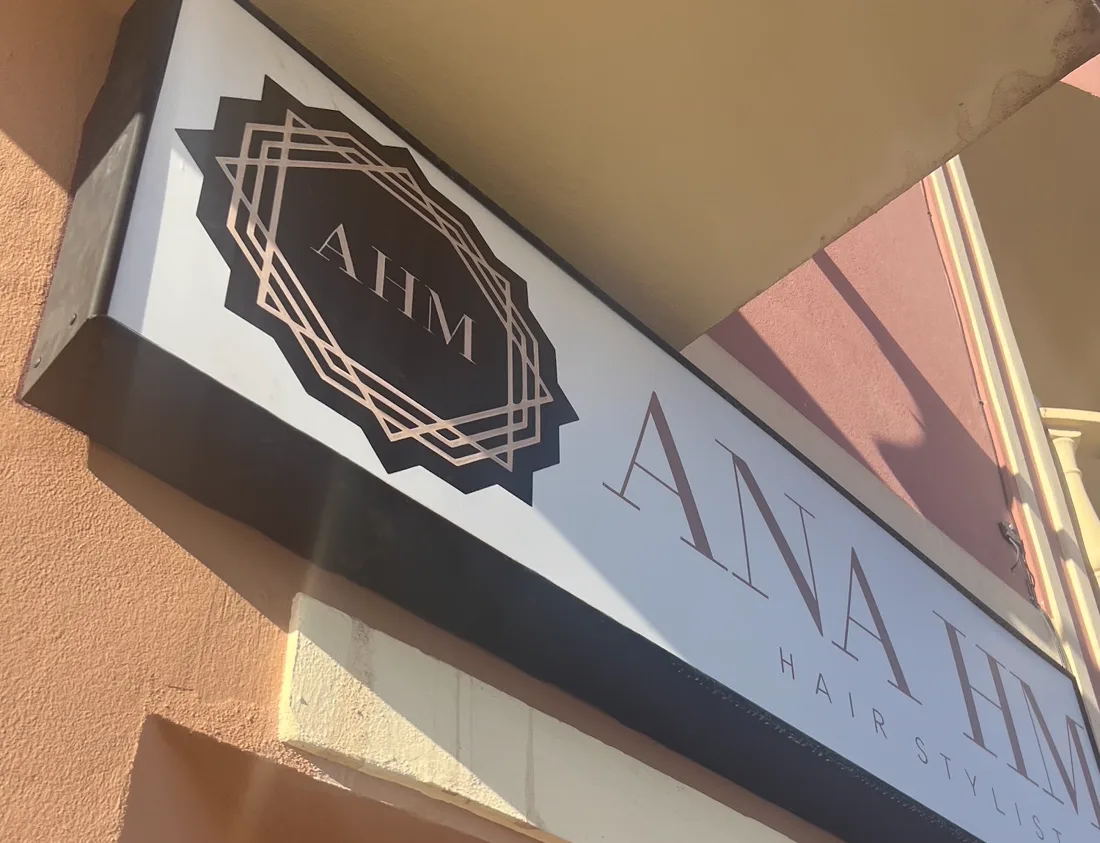 El rótulo de la entrada: el monograma AHM en un sello geométrico de líneas de cobre, junto al nombre Ana HM Hair Stylist.